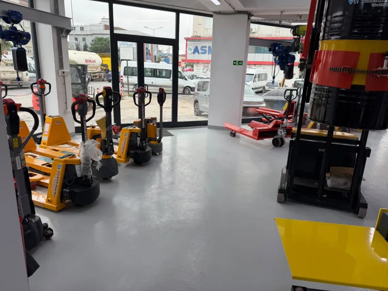 Yellow electric pallet trucks lined up at the shop entrance, with a scissor pallet truck and a drum lifter on the right