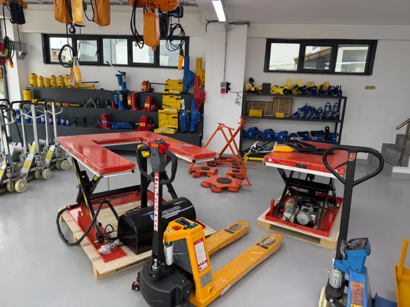 U-shaped and standard scissor lift tables, orange machine skates and plate lifting clamps on the shelf, with an electric pallet truck in front
