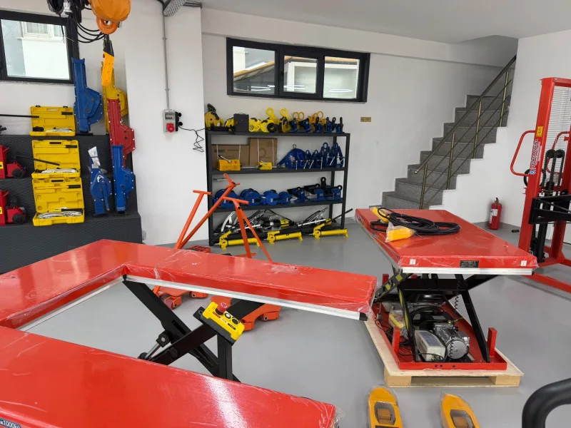 Plate lifting clamps, lifting magnets and hydraulic hand pumps on the shelf, with scissor lift tables in front and mechanical jacks on the left
